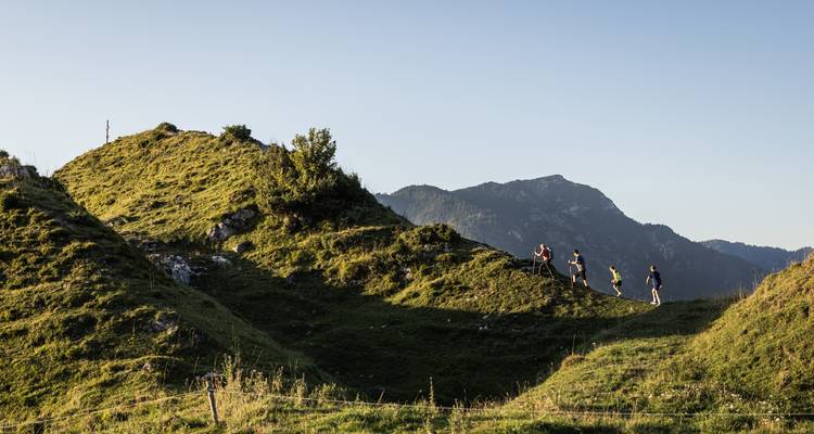 Des gens faisant de la randonnée le long d'une crête herbeuse avec un paysage de montagnes en arrière-plan.