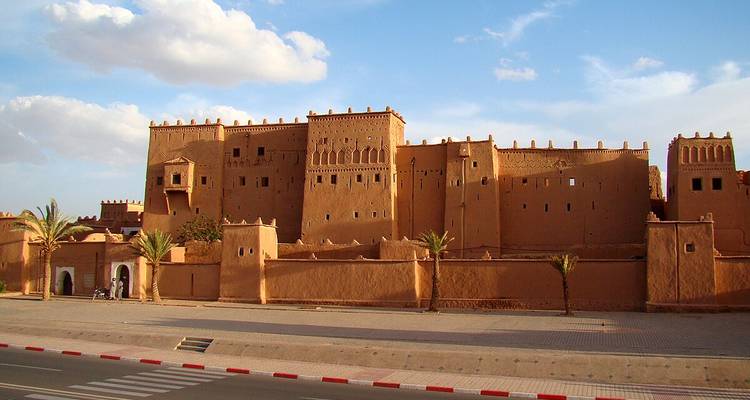 Grande kasbah avec palmiers et ciel dégagé.