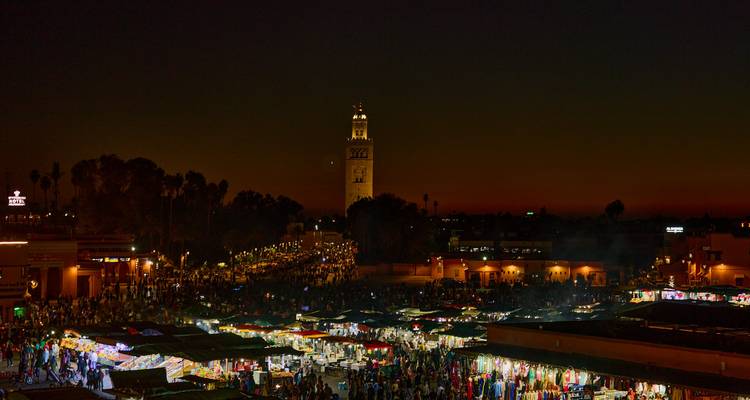 Marché animé de Marrakech la nuit avec éclairage et une haute tour.