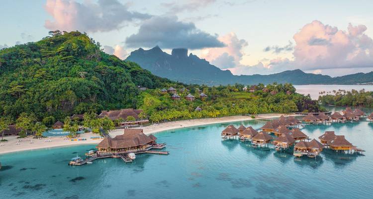 Île tropicale avec montagnes et bungalows sur pilotis.