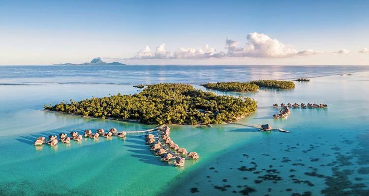 Vue aérienne d'une île tropicale avec des bungalows sur pilotis.