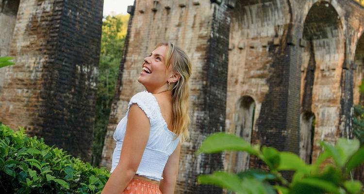 Un voyageur joyeux sourit à côté des hautes arches de brique d'un viaduc historique entouré de verdure de jungle