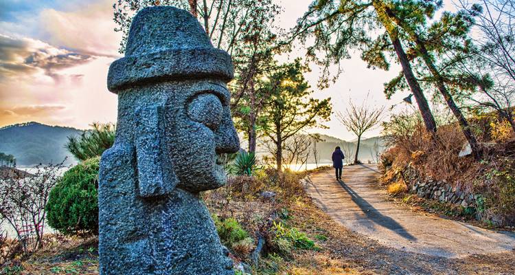 Steinstatue in einem malerischen Park mit einer Person, die im Hintergrund spaziert.