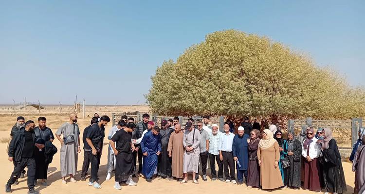 Groupe de personnes incluant des hommes en vêtements traditionnels debout près d'un arbre.