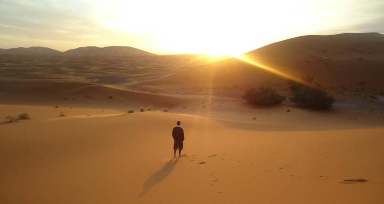 Sunset over sand dunes with a lone figure.