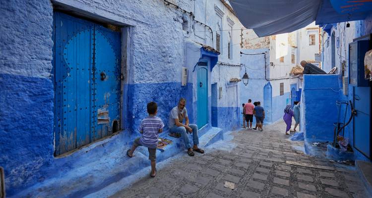 Blue-walled street with people and traditional doors.