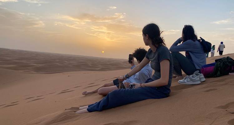 Un groupe de personnes assises sur des dunes de sable regardant le coucher de soleil.