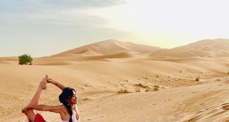 Personne pratiquant le yoga sur des dunes de sable sous un soleil éclatant.