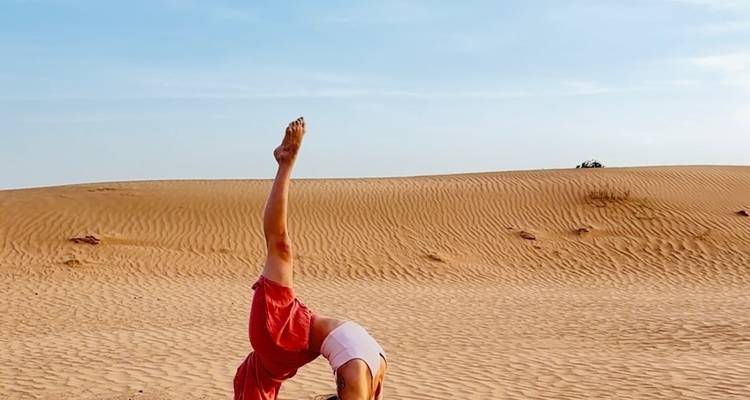 Personne dans une pose de yoga au milieu d'un désert de sable.