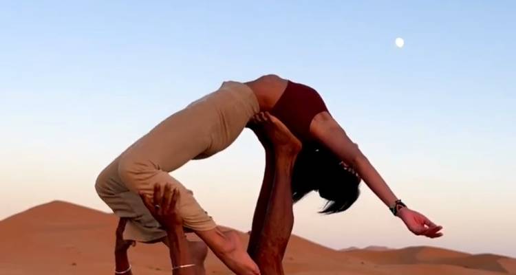 Zwei Personen führen eine Acroyoga-Pose in der Wüste aus.
