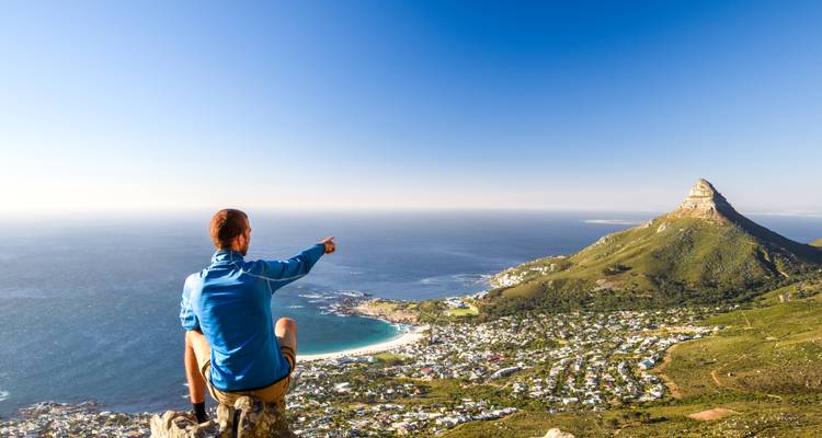 Person, die auf einer Klippe sitzt und auf Ozean und Berge blickt.