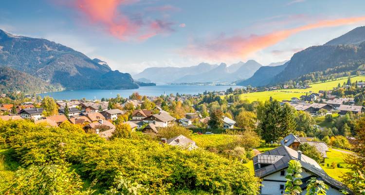 Un village avec des champs et des montagnes sous un ciel coloré au coucher du soleil.