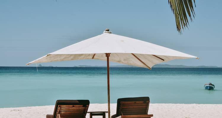 Plage avec deux chaises sous un parasol face à la mer.