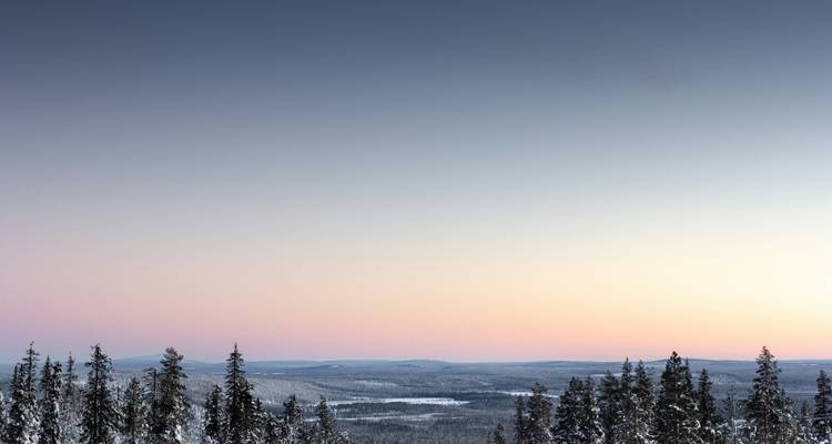 Paysage enneigé avec des collines lointaines sous un ciel coloré.
