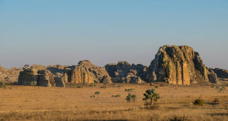 Vaste paysage avec des formations rocheuses escarpées et une zone de prairie sèche sous un ciel dégagé.