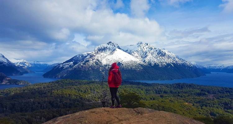 Personne en veste rouge debout sur un rocher avec une vue sur une montagne enneigée.