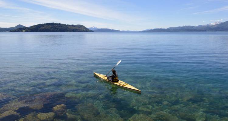 Personne faisant du kayak sur un lac calme avec des montagnes en arrière-plan.