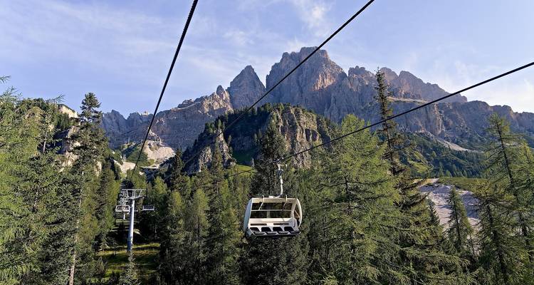 Sessellifte gleiten über grünen Lärchenwald auf imposante Felsgipfel in den Dolomiten zu.