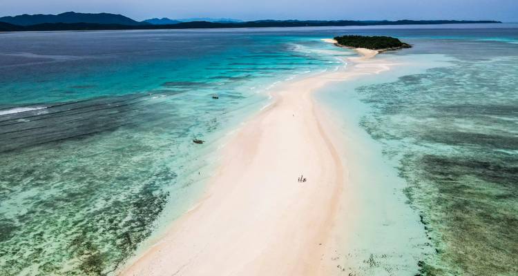 Luchtfoto van een wit zandpad dat leidt naar een tropisch eiland omringd door turquoise water.