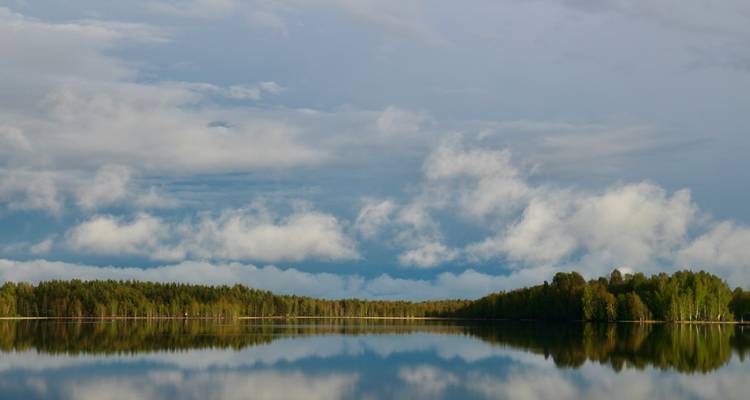 A serene lake with reflections of clouds and trees.