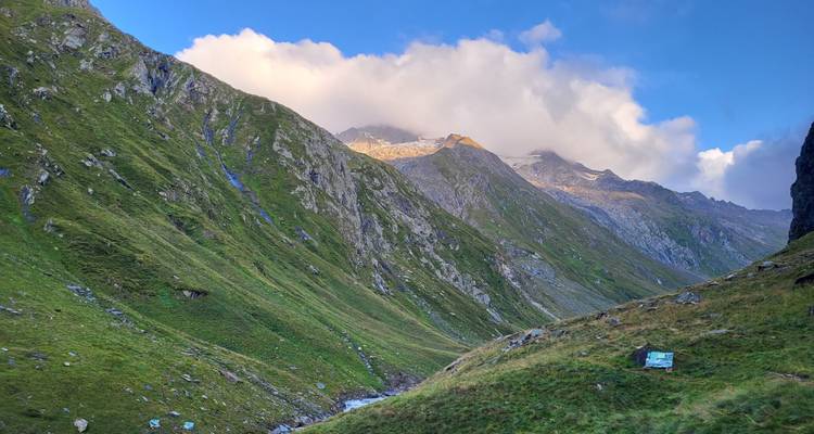 Ein üppiges grünes Bergtal unter einem dramatischen bewölkten Himmel.