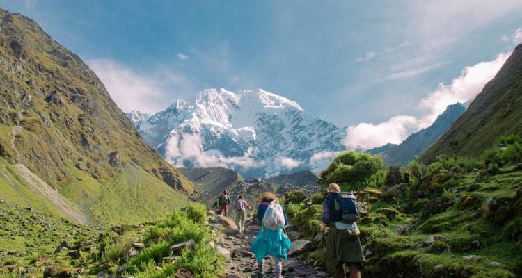Randonneurs gravissant une vallée verdoyante avec un sommet enneigé devant eux.