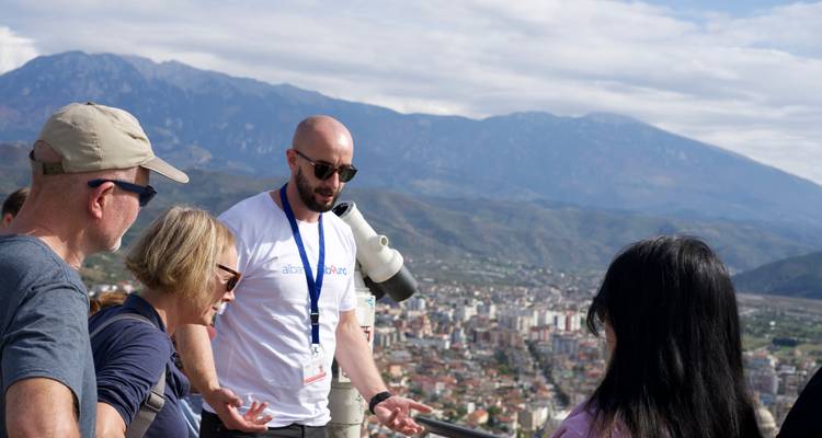Reiseführer erklärt einer Gruppe mit Panoramablick auf eine Stadt und Berge.