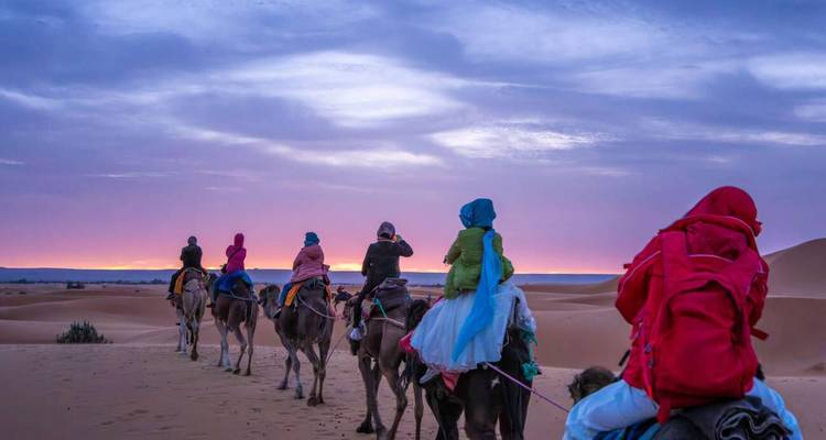 Des personnes chevauchant des chameaux dans le désert au coucher du soleil, Maroc.