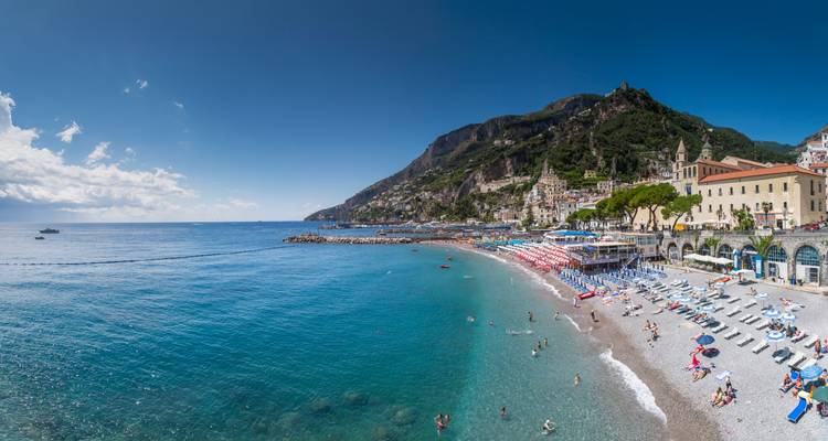 Vue panoramique de la plage de galets d'Amalfi, de la mer turquoise et de la ville hillside sous un ciel dégagé.