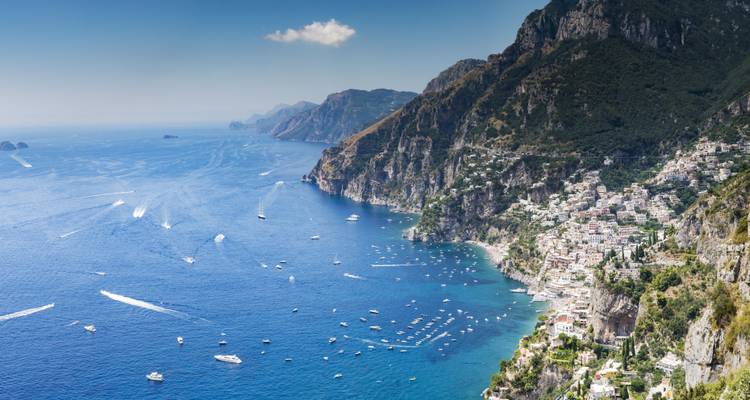 Vue aérienne panoramique de la côte amalfitaine montrant les maisons en falaise de Positano et la mer bleue étincelante parsemée de bateaux.