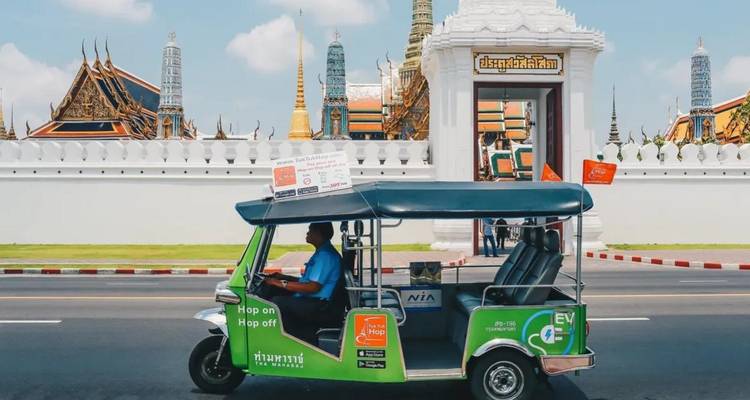 Un tuk-tuk frente a la entrada de un templo con torres doradas.