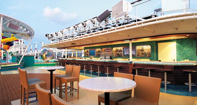 Área de bar al aire libre en un crucero, con asientos y un cielo despejado arriba.