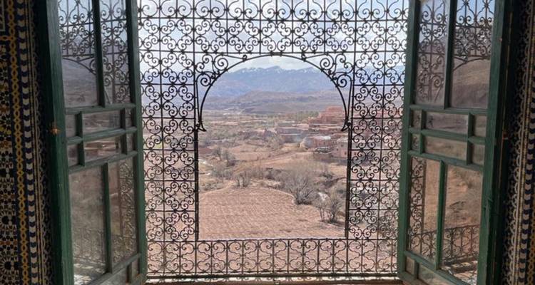 Malerische Aussicht durch ein kunstvoll gestaltetes Fenster über ein Tal und Berge.