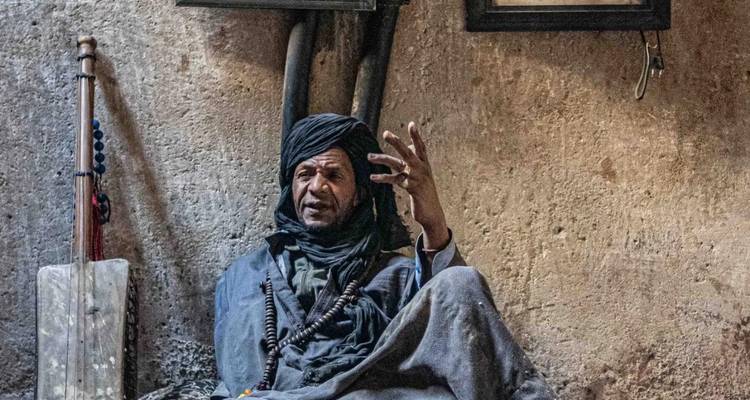 Ein Mann in traditioneller Kleidung spricht in einem schwach beleuchteten Raum.