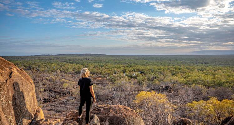 Person standing on rocks overlooking a vast, green landscape.