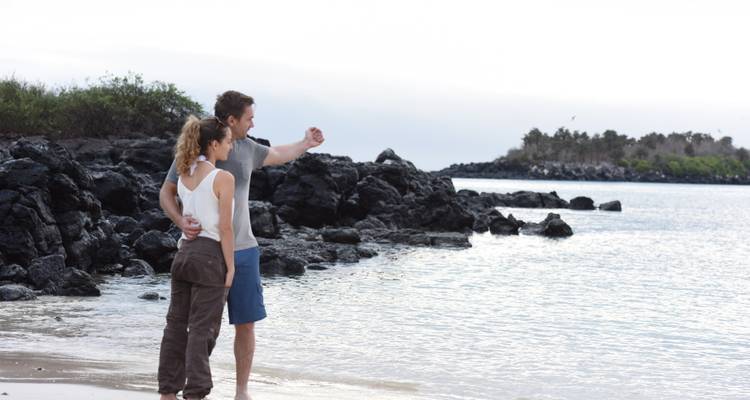 Een stel dat dicht bij elkaar staat en vanaf een rotsachtige kust naar de zee kijkt.