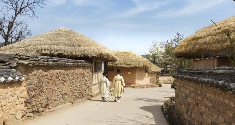 Twee mensen in traditionele Koreaanse klederdracht die voorbij oude huizen lopen