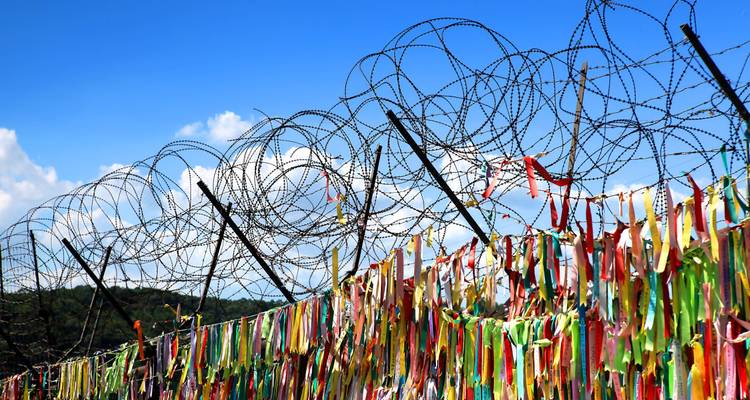 Kleurige linten op prikkeldraad hek met blauwe lucht.