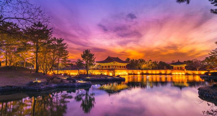 Historisch paviljoen weerspiegeld in het rustige water van de Anapji-vijver onder een dramatische oranje-paarse zonsonderganghemel.