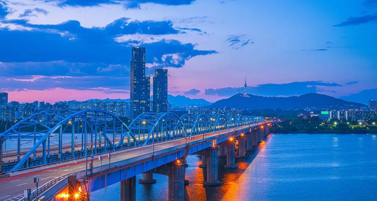 Blaue Stunde Blick auf eine beleuchtete Brücke, die den Han-Fluss überspannt in Richtung Seouls moderner Skyline mit dem Namsan Seoul Tower auf einem entfernten Hügel.