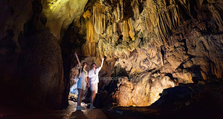 Des personnes explorant une grotte bien éclairée avec des stalactites.