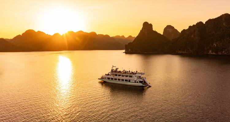 Bateau de croisière naviguant pendant un coucher de soleil pittoresque avec un arrière-plan vallonné.