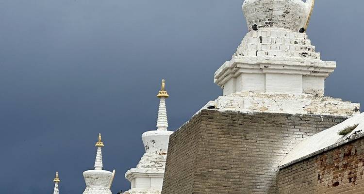Reeks witte stoepa's met gouden punten opgesteld naast een oude bakstenen muur onder donkere luchten.