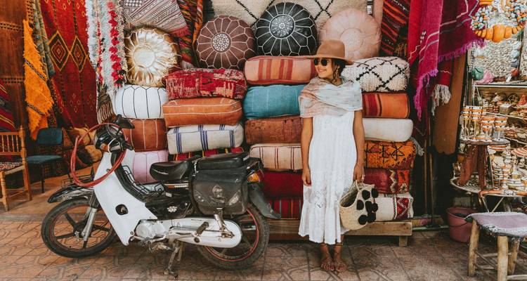Une femme posant à côté d'une variété de tissus marocains traditionnels exposés dans un marché de rue.
