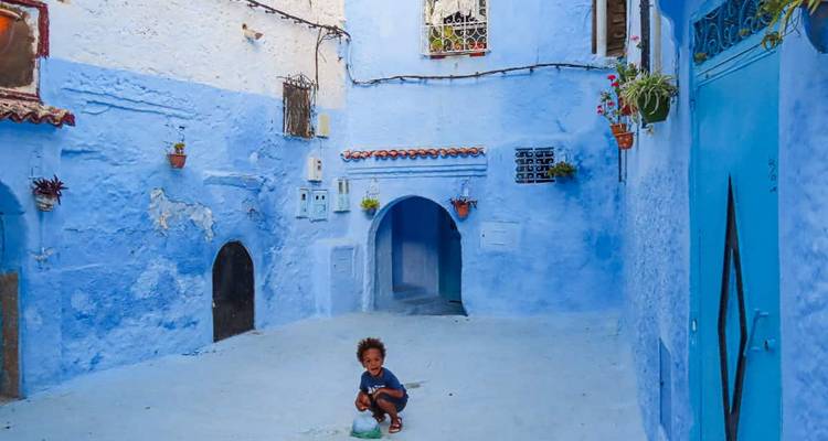 Un enfant jouant dans les rues peintes en bleu de Chefchaouen, avec des bâtiments blancs et bleus alentour.
