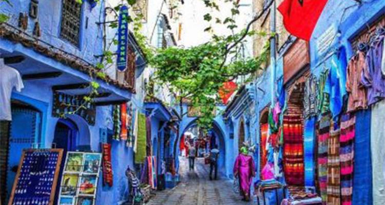 Une ruelle animée à Chefchaouen avec des murs bleus, des boutiques colorées et des vignes qui pendent au-dessus.
