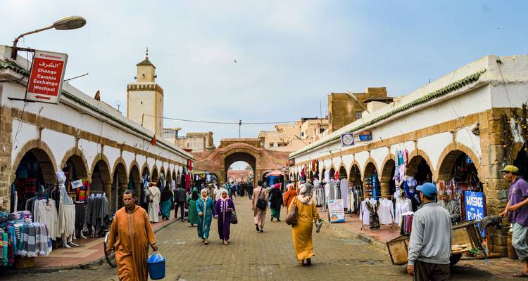 Des gens marchent dans un marché traditionnel marocain avec des passages voûtés et des boutiques de chaque côté.