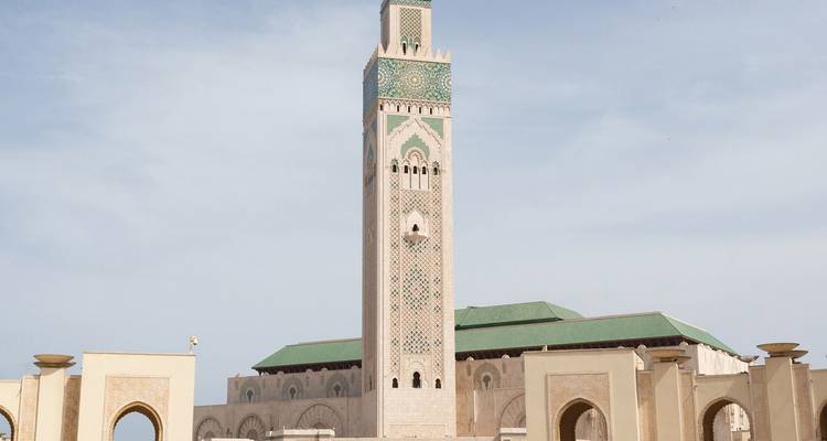 Alto minarete de la Mezquita Hassan II enmarcado por arcos bajo un cielo azul pálido.