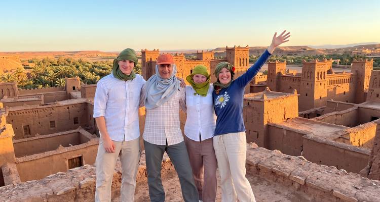 Quatre voyageurs portant des foulards célèbrent au coucher du soleil sur les toits de kasbah en brique de terre.