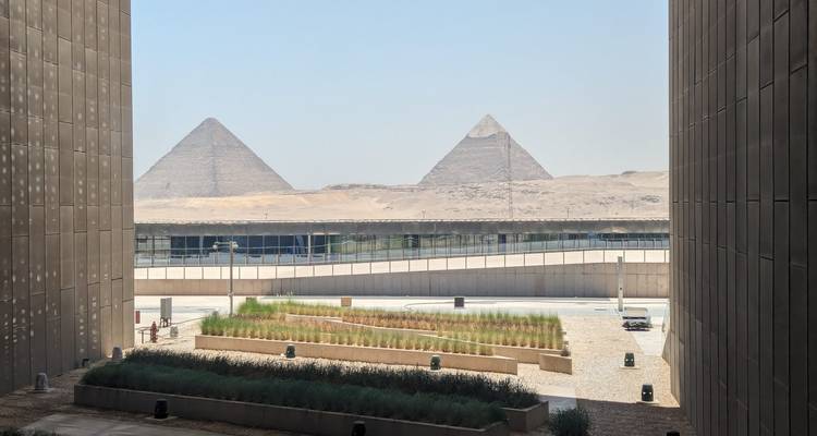 Vue entre des bâtiments modernes montrant des pyramides en arrière-plan.